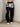 Woman wearing a white crop top and black sweatpants with 'SMD' text, standing against a plain wall.